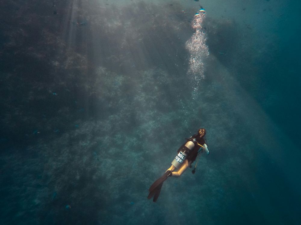 sun ray under water and a female scuba diver swimming