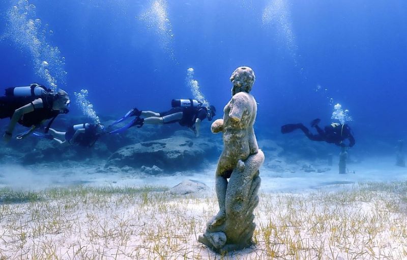 three scuba divers looking at a statue underwater