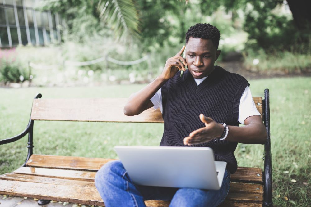 a guy talking on phone with laptop on lap
